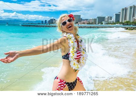 Female enjoying showing her hawaiian lei necklace. Freedom woman with american flag bikini and white garland orchids. Waikiki Beach, Honolulu, Oahu in Hawaii. Tropical destination holiday travel.
