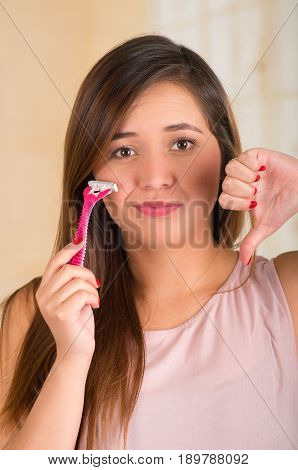 Close up of a beautiful young funny woman with an shaver on her face with a thumps down.