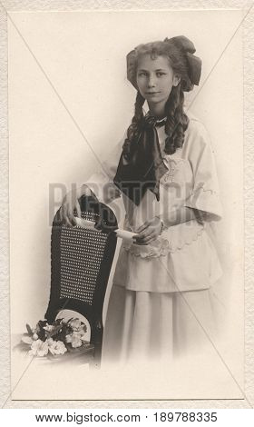 HARRISON, IDAHO, USA - CIRCA mid-1910s: Vintage portrait of a young girl in ringlet curls holding a diploma