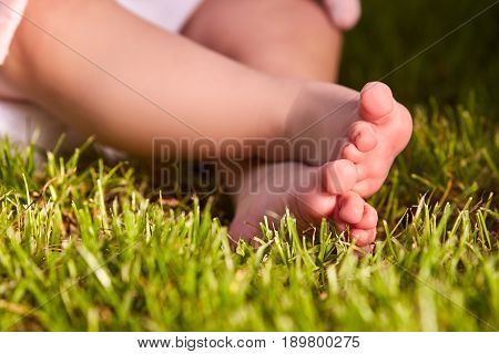 Small baby feet on the green grass at summer sunshiny day in the park. Cute baby in the white clothing. Horizontal croped photo. Concept of the happy babies.
