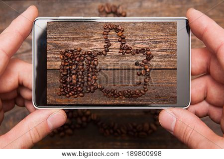 Social network. Mobile food photography. Thumbs up made by coffee beans. Popular shape for communication and advertisement on wooden background , top view