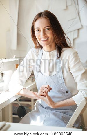 Portrait of beautiful seamtress wearing blue apron sitting in workshop