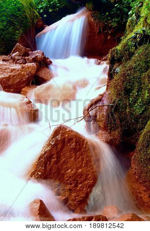 Cascades In Rapid Stream Of Mineral Water. Red Ferric Sediments On Big Boulders
