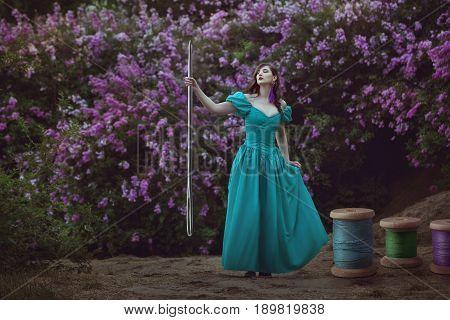 Fairy-tale woman holds a large needle in her hand next to large coils with threads.