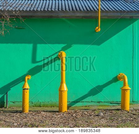 Yellow gas pipes in front of green building wall. Fragment of gas distribution station