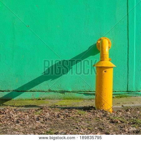 Yellow gas pipe in front of green building wall. Fragment of gas distribution station
