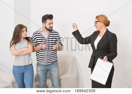 Realtor proposing to sign a cotract to man and woman. wha are not agree. Happy estate agent insisting on signing agreement. Young couple hesitating to sign up rent agreement.
