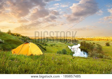 view of tourist tent on green meadow at sunrise or sunset. Camping background with copy space. Tent on the hill near the river. Adventure travel active lifestyle freedom concept. Summer landscape