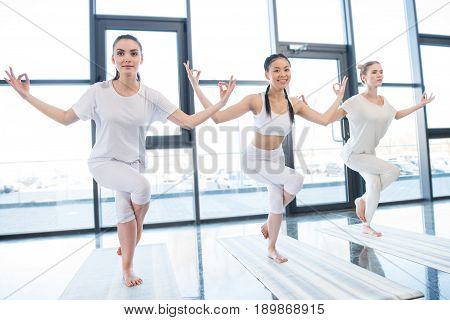 Smiling young women practising Garudasana Eagle Pose at yoga class