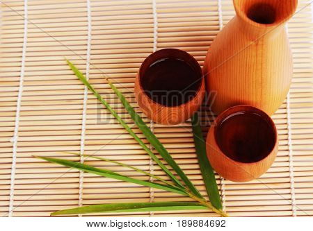 SAKE liqueur in a brown wooden bottle on a light brown background.