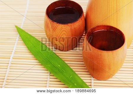 SAKE liqueur in a brown wooden bottle on a light brown background.