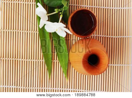 SAKE liqueur in a brown wooden bottle on a light brown background.