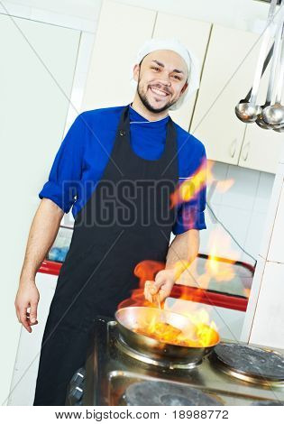 พ่อครัวคนในเครื่องแบบทำ flambe อาหารกับกระทะในครัว