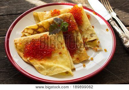 Maslenitsa traditional Russian pancakes - blini with red caviar on a white plate of wood table