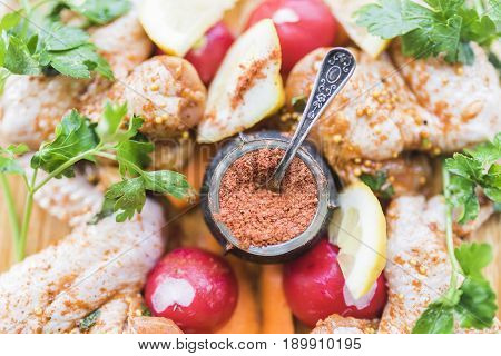 Fresh chicken wings vintage carved pepper with spices lemon slices red radish bright green parsley lie on a wooden cutting board.