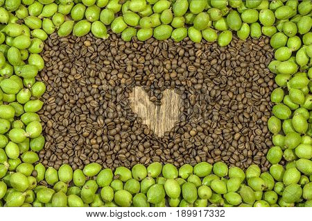Picture frame made of green young walnuts in husks and inside a lot coffee bean with hert on wooden table