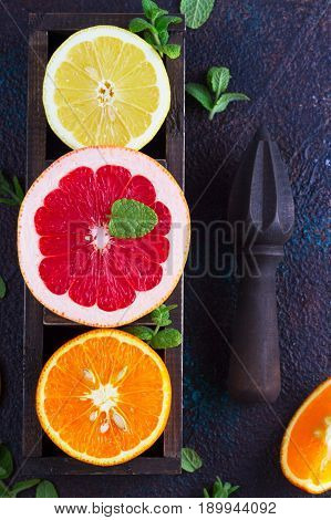 Orange, lemon and grapefruit with citrus reamer on dark background