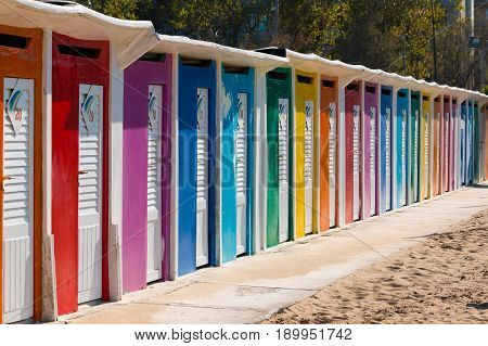 A row of beach huts with brightly coloured doors on sandy beach Rimini Italy