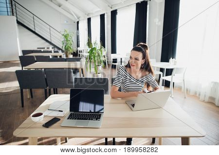 Young attractive woman at a modern office desk, working with laptop, looking away, thinking about a post, full-time blogger, seeking for inspiration