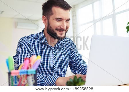 Close-up of pleasant male in blue checkered shirt working with laptop