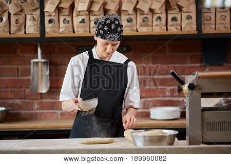 Female cook in uniform putting floor on dough while cooking pasta in cafe. Making pasta. Making pasta in restaurant. Woman add flour to dough