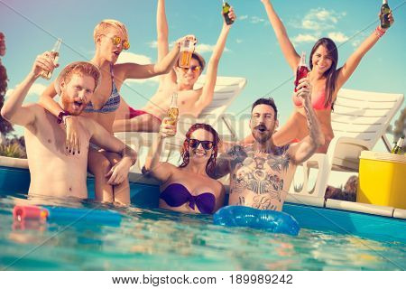 Happy boys and girls in pair enjoying in piscine with beverage in hands