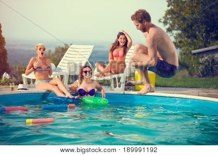 Male jump style bomb in open pool while girls admires him