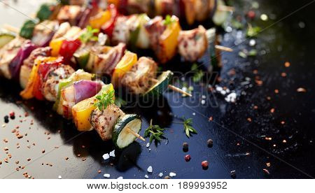 Grilled meat and vegetable skewers with fresh herbs and spices, dark background
