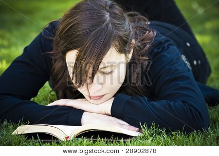 美しいブルネットの女性は草の上を読んで