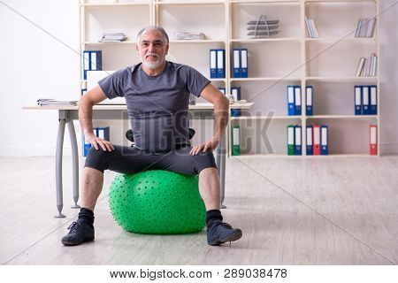 White bearded old man employee doing exercises in the office 