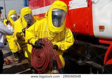 Three Firefighters In Protective Suits And Gas Masks Are Preparing To Extinguish The Fire. Mechanism