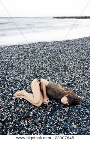 美しい女性の悲しいジェスチャーで浜辺を敷設します。長い露出の波。