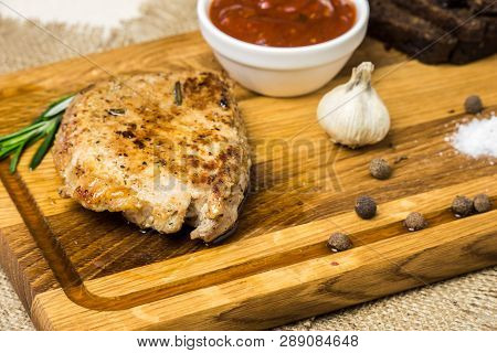 Pork Chop Lies On A Board With Spices, Garlic, Rye Bread, Baked Vegetables And Sauce.