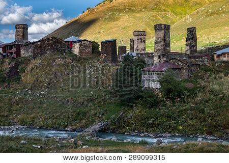 Mountain Murkmeli Village In Ushguli Community With River Under It And Bridge And Sunny Meadows