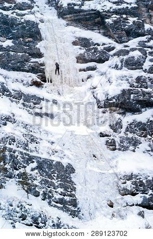 Ice Climber Climbs A Icefall On A Cliff During A Snowfall