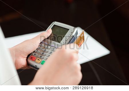 Hand Swiping Debit Card On Pos Terminal. Business People In Office Holding A Conference And Discussi