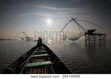 Asian Fisherman On Wooden Boat Casting A Net For Catching Fish In Nature River In Morning Before Sun