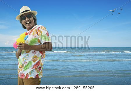 Happy Elderly Traveler Asian Man Wearing Summer T-shirt, Straw Hat And Sunglasses Holding Colorful W