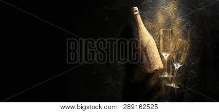 Photo of golden champagne bottle, two wine glasses on black stone background