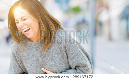 Beautiful middle age woman wearing winter sweater over isolated background Smiling and laughing hard out loud because funny crazy joke. Happy expression.