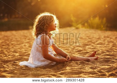 Little Happy Girl Sitting And Playing In The Sand On The Beach