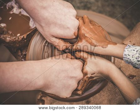 Teaching Pottery A Carftmans Hands Guiding A Child Hand, Showing How To Throw A Clay Pot On A Potter