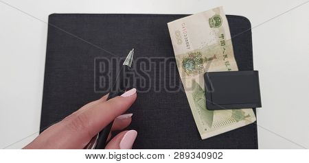 Female Hand Holding Black Pen On Black Folder With One Chinese Money Banknote