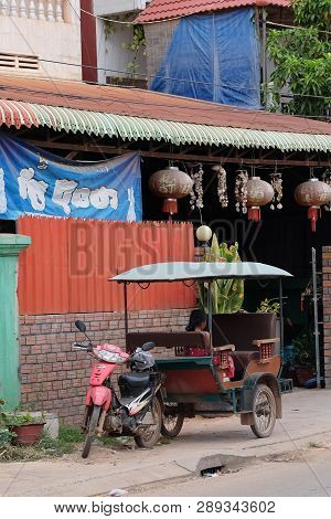 Cambodia, Siem Reap 12/08/2018 A Little Asian Girl Sits In A Moto Rickshaw Near A House With Red Lan