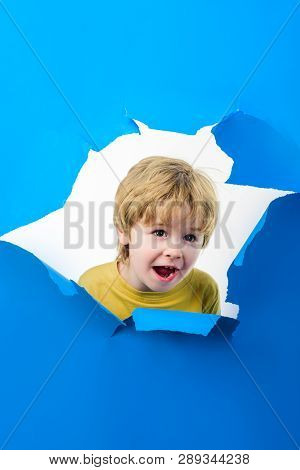 Smiling Boy Looking Through Hole In Paper Wall. Happy Child Boy Making Hole In Paper. Kid Looks Thro