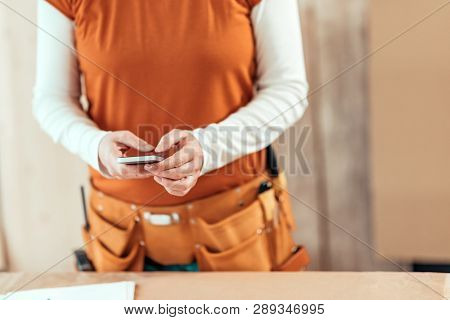 Female Carpenter Is Using Mobile Phone For Text Messaging, Close Up Of Hands Typing Sms On Smartphon