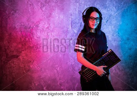 Young Sexy Disco Girl Wearing Gaming Headset Holding Gaming Keyboard. Room Lit In Retro, Retrowave O