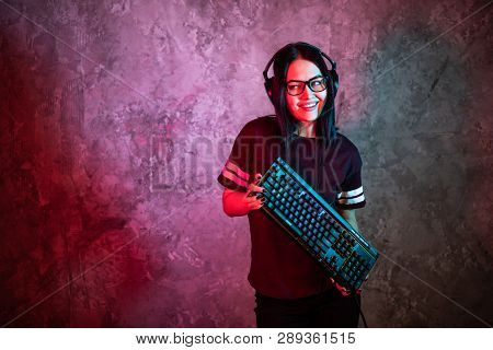 Young Sexy Disco Girl Wearing Gaming Headset Holding Gaming Keyboard. Room Lit In Retro, Retrowave O