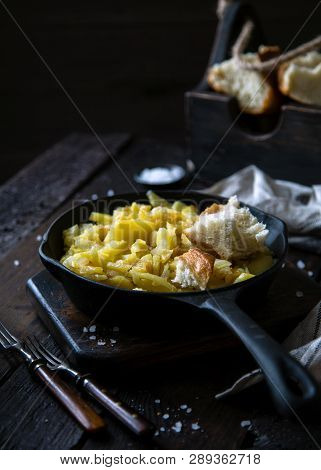 Homemade Roast Potatoes In Cast-iron Pan Standing On Wooden Board On Rustic Dark Wooden Table With P