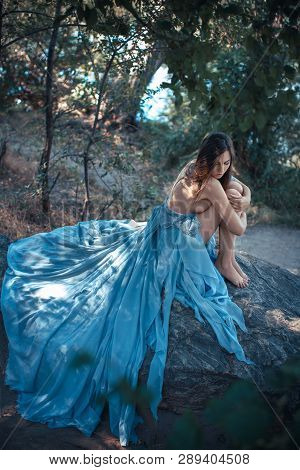 Fashion Art Photo. Sexy Attractive Woman With Naked Breast And Back In Blue Dress Sitting On Rocky B